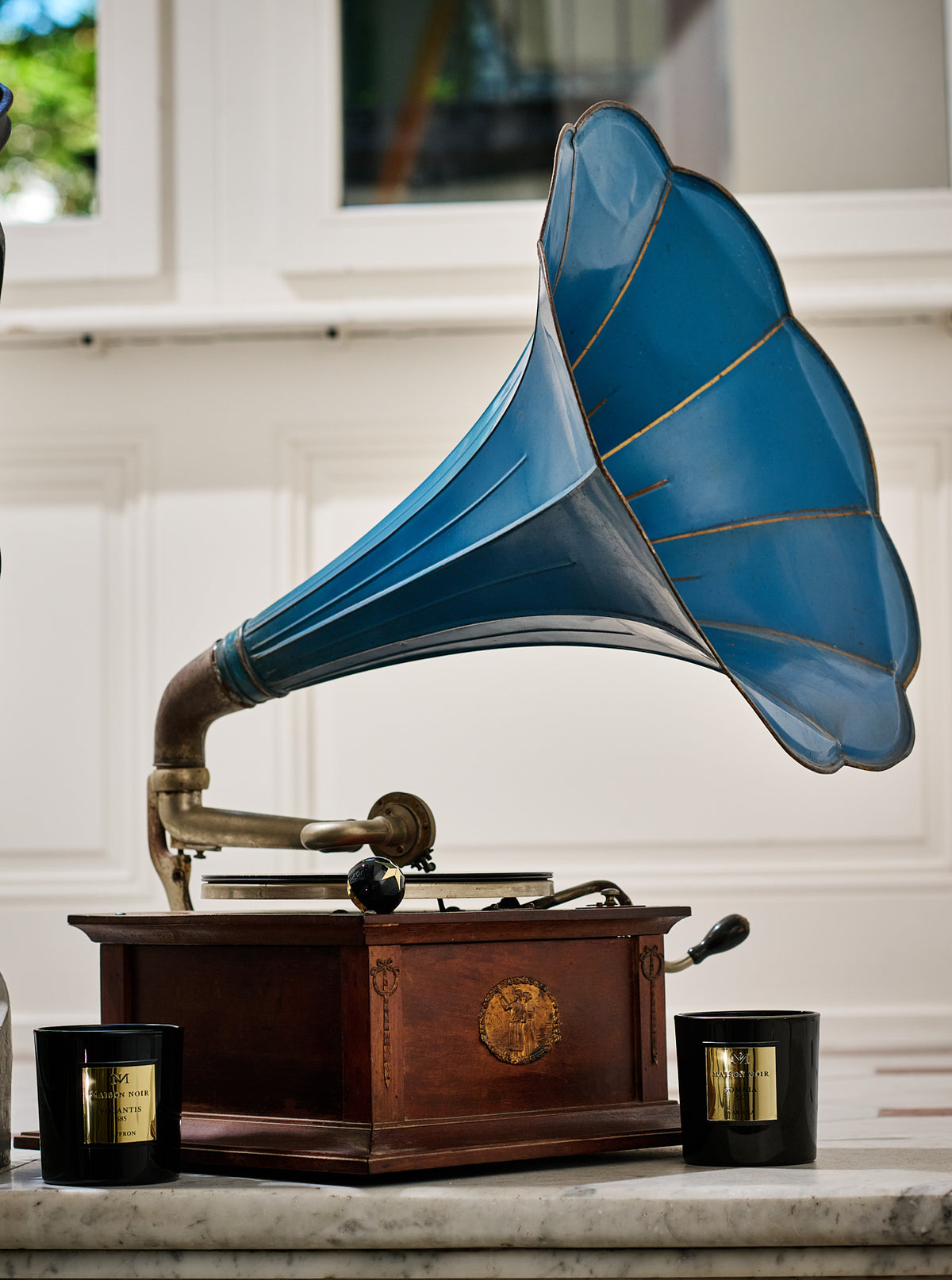 A blue-horn gramophone beside black and gold Maison Noir candles